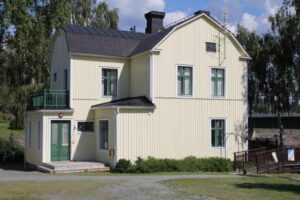 The yellow wooden hostel house with green windows on a sunny summer day