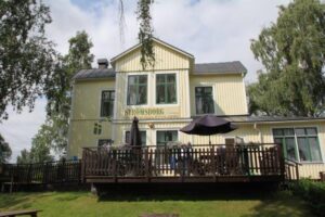 Det gula trähuset Strömsborg med altan och parasoll, sett från gräsmattan